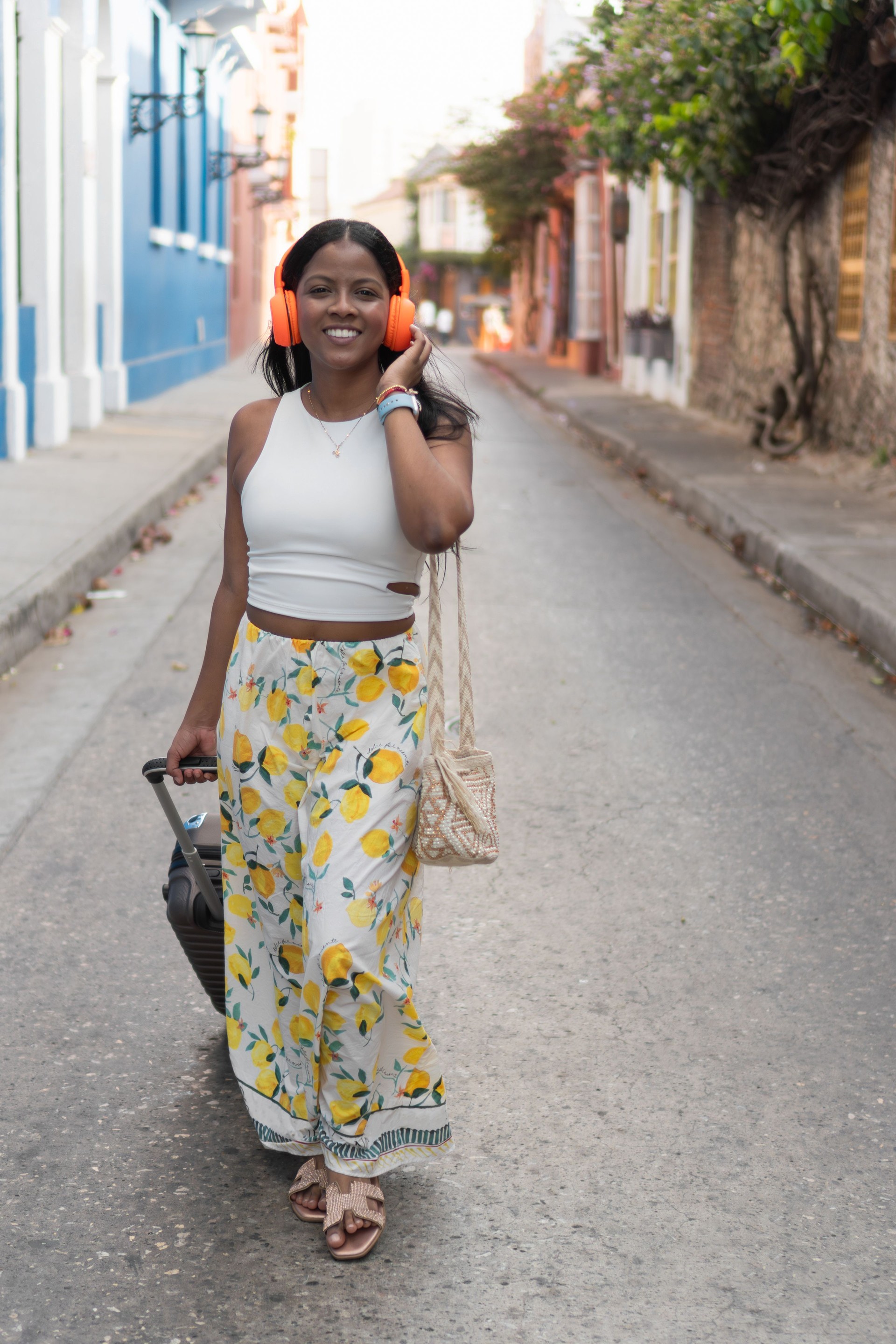 Young tourist walking down the street listening to music with headphones and pulling suitcase